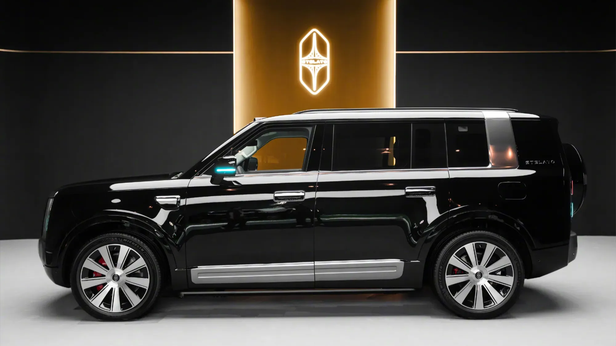 Stelato G9 shown in black from the side, parked in a studio beside an illuminated logo pillar