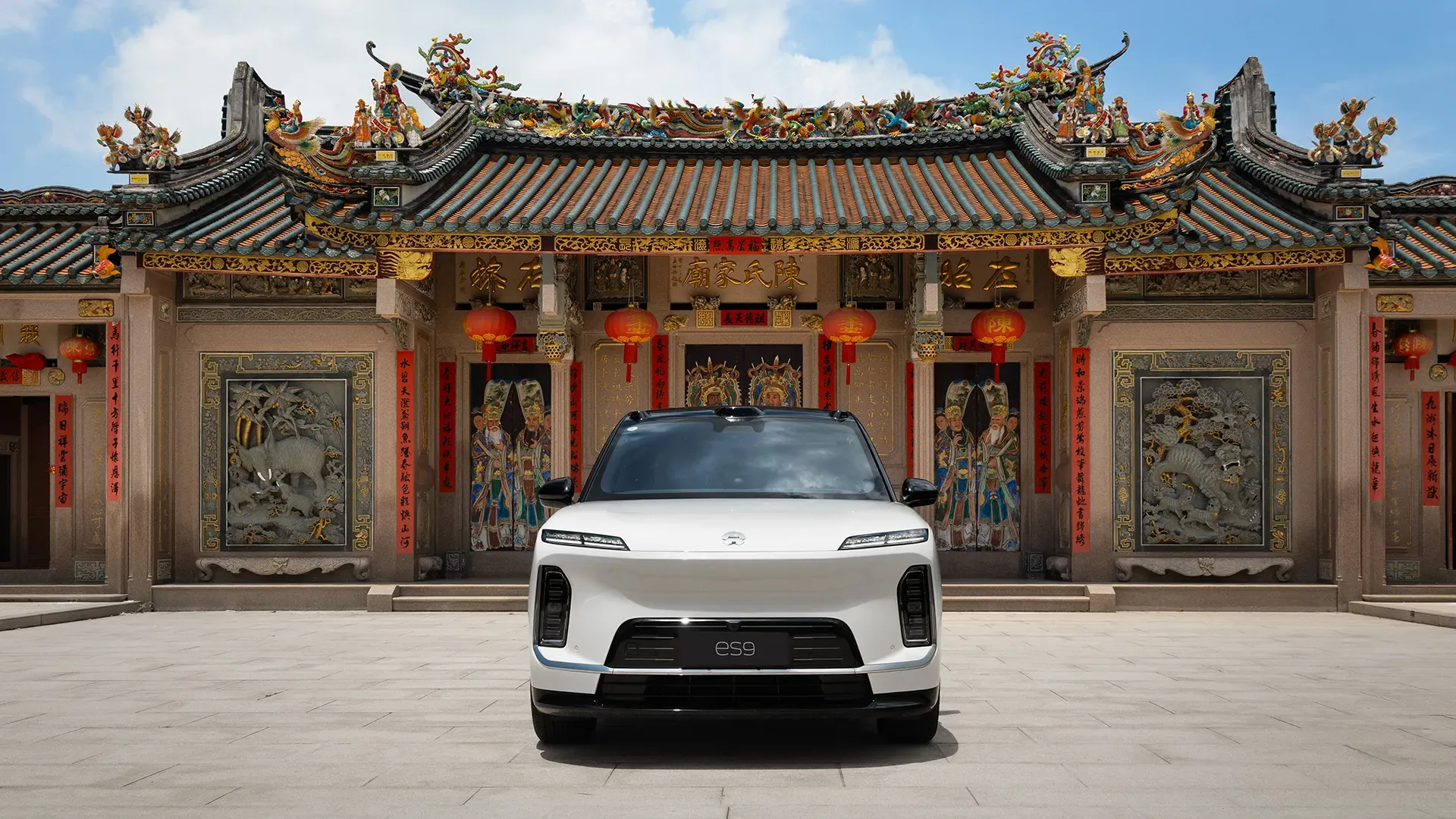 White NIO ES9 posed head-on in front of an ornately carved Chinese temple with dragon-topped eaves and red lanterns.