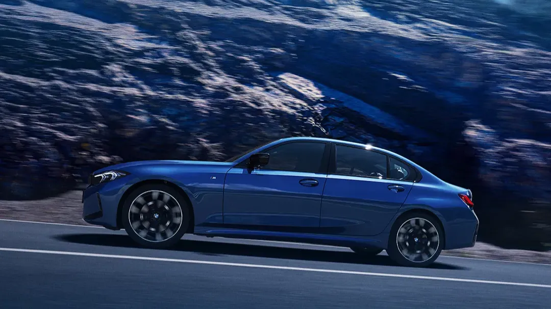 Blue current-generation BMW 3 Series sedan cornering on a mountain road, shown in profile