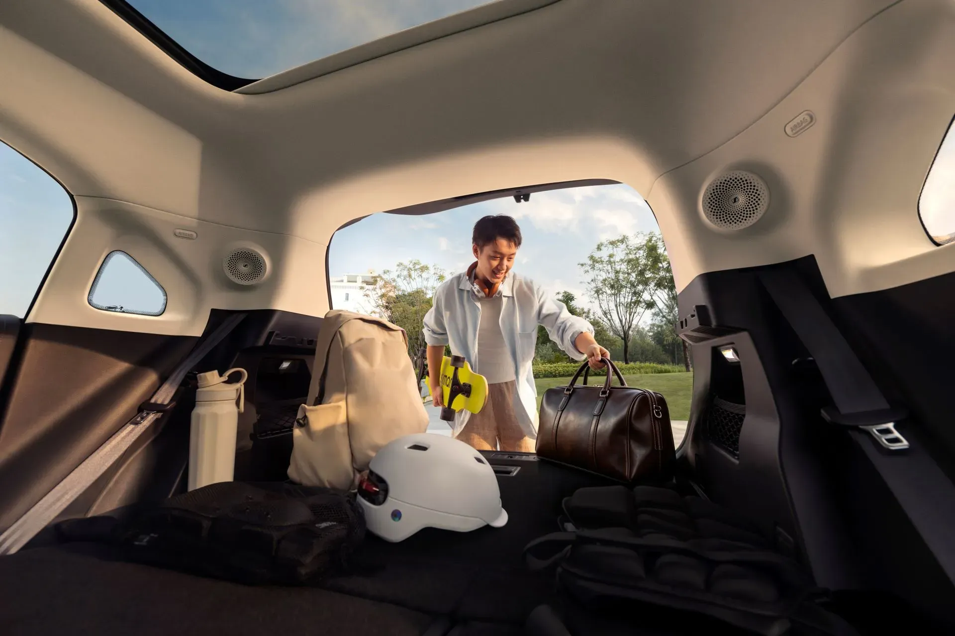 Open cargo area of the new smart #1 loaded with a backpack, helmet and skateboard as a passenger adds a duffel bag.
