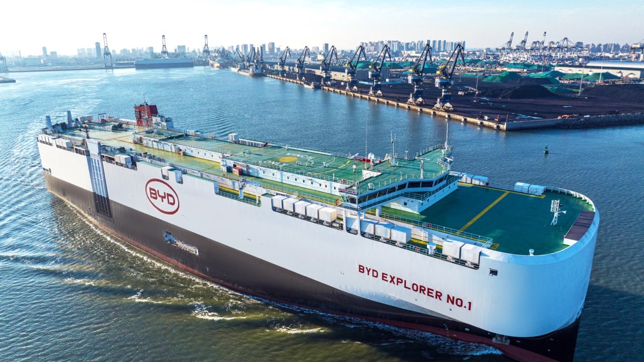 BYD Explorer No.1 car carrier sailing past an industrial port with the brand logo on its hull
