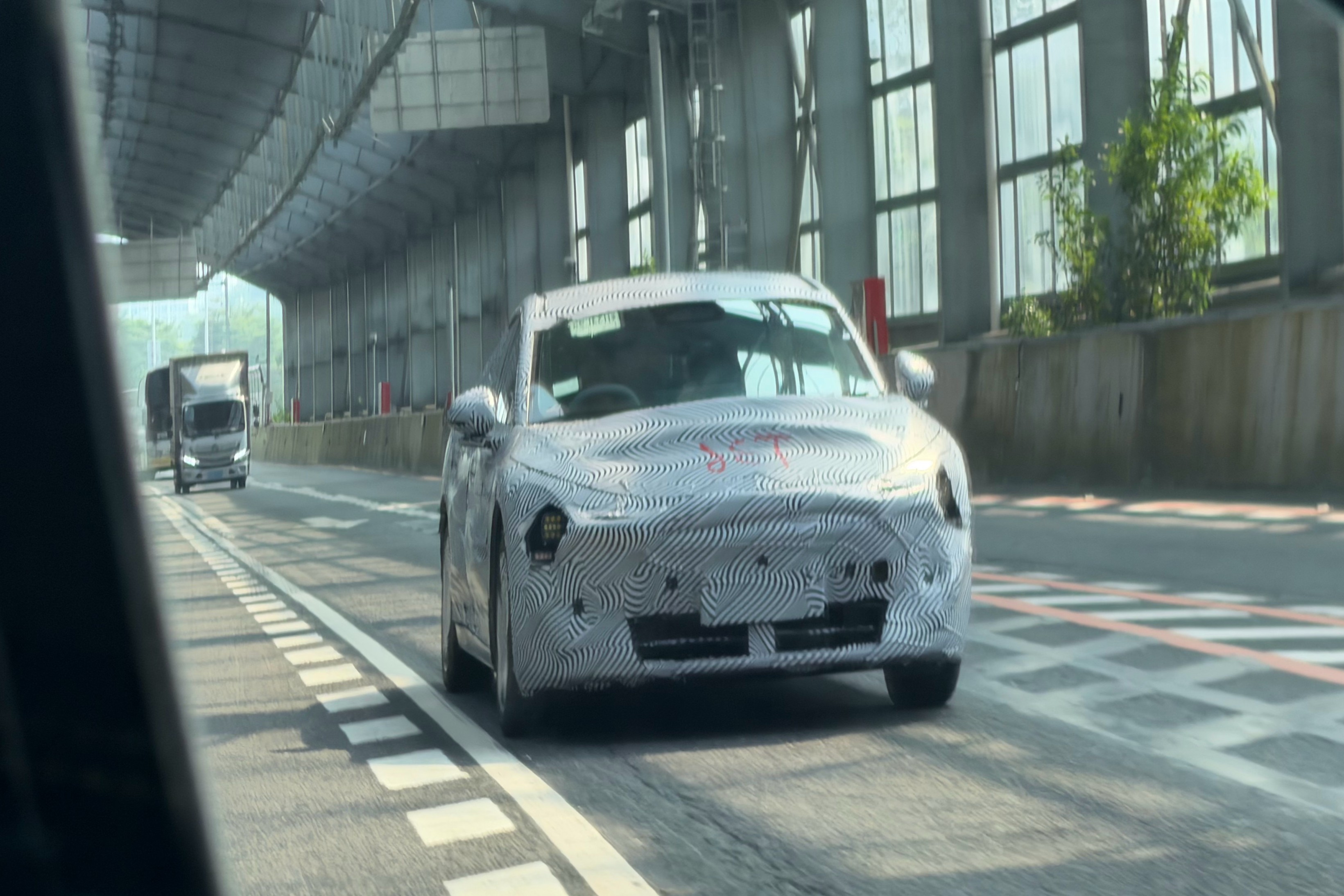 Camouflaged XPeng Mona D11T wagon prototype driving through an underpass in Guangdong, China, front three-quarter view