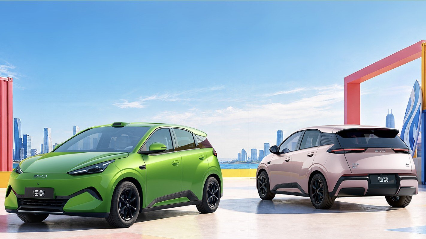 Lime green and pink second-generation BYD Seagull hatchbacks parked on a waterfront plaza with a city skyline behind