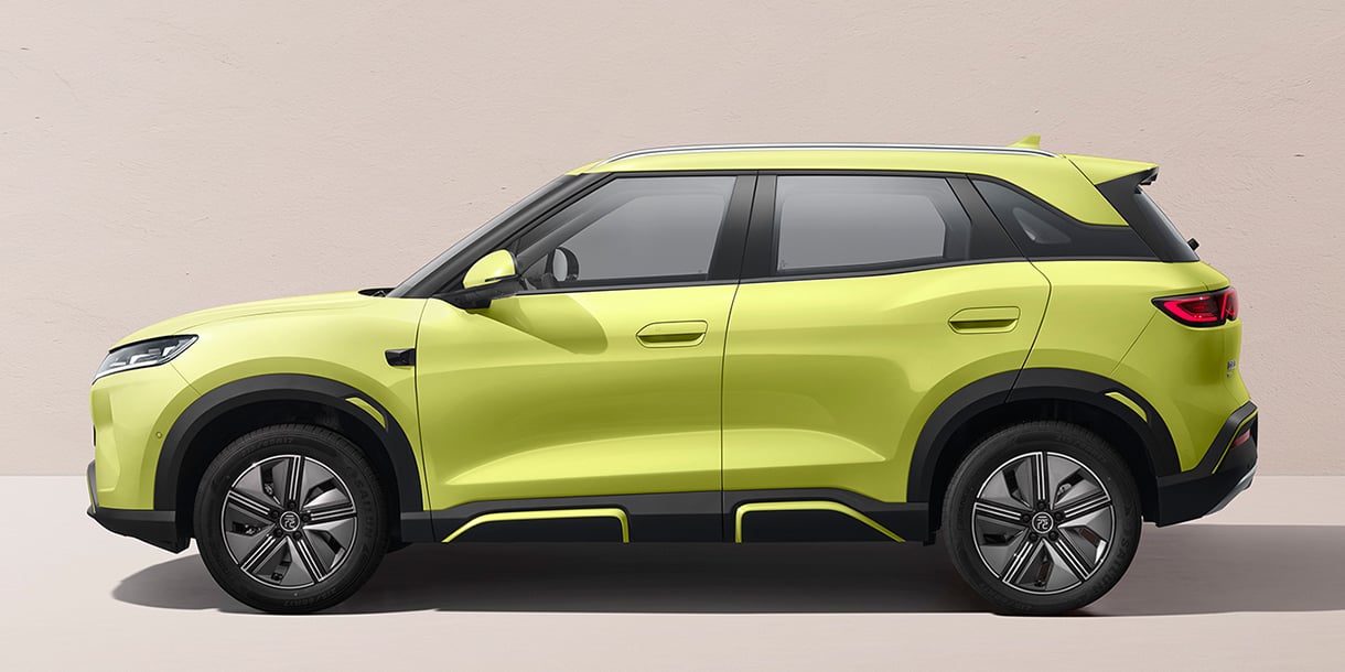 Side profile of a yellow-green BYD Yuan UP Feichi edition compact SUV with black wheel arches against a plain beige wall