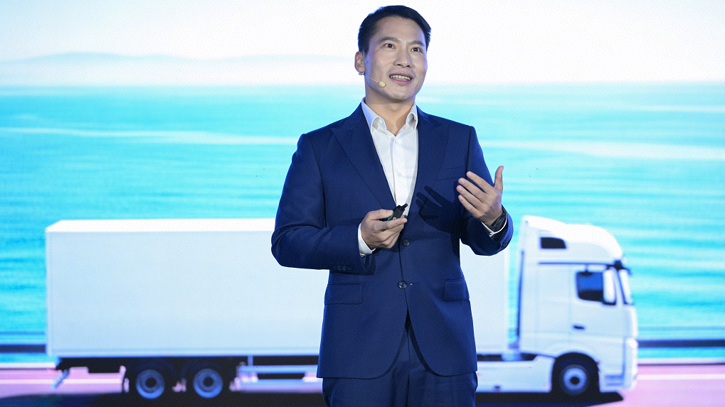CATL overseas business head Akin Li speaking on stage in front of a projected white electric truck