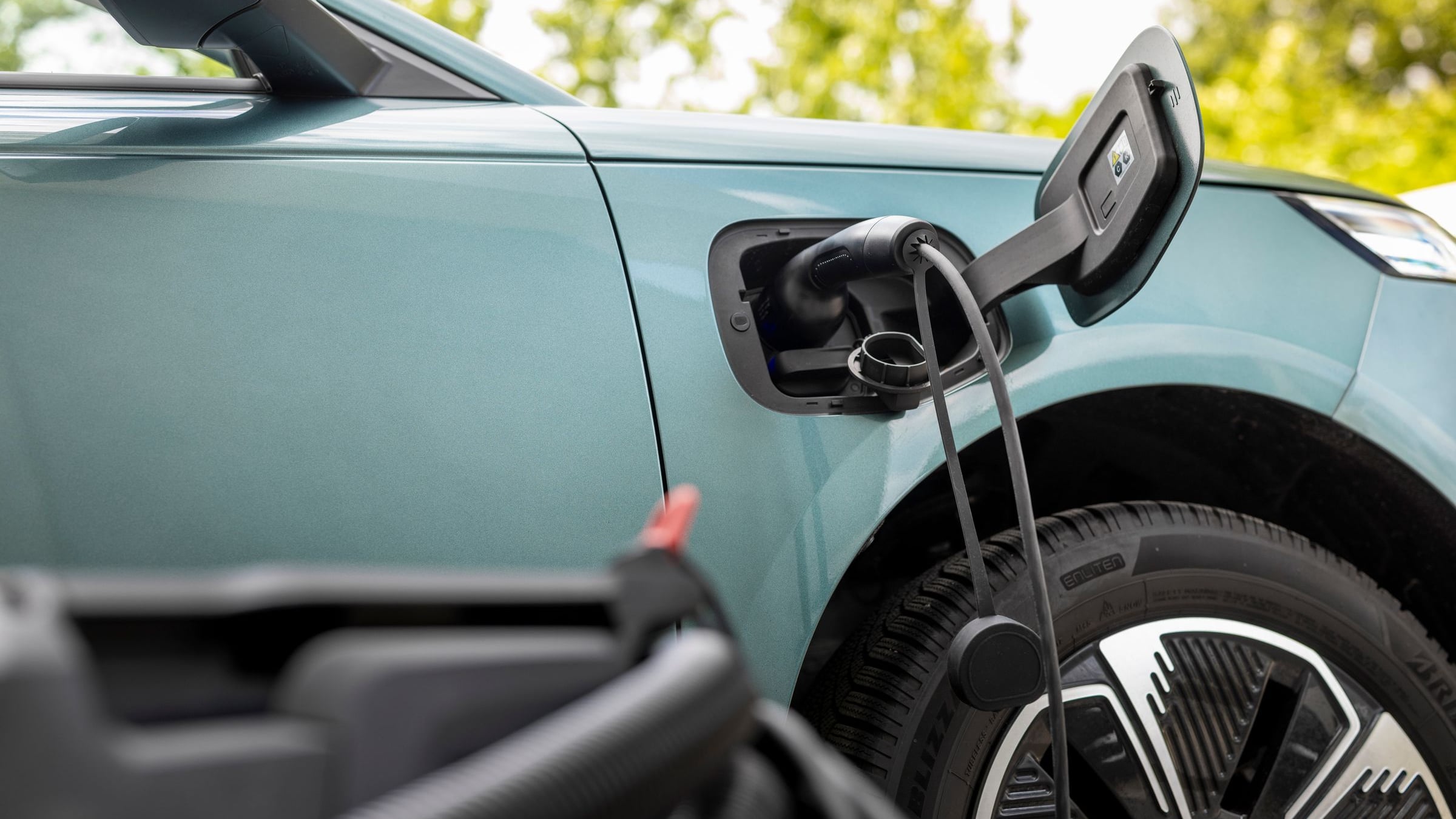 Charging cable plugged into the front-wing charging port of a green Jaecoo J5 EV, with the port flap open