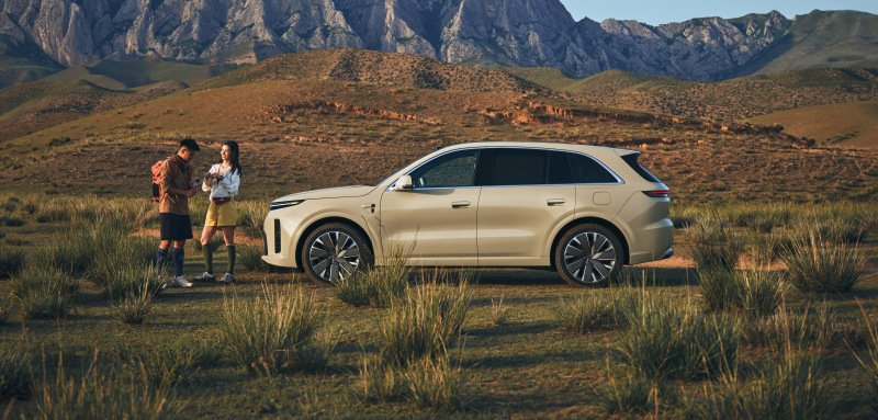 Champagne Li Auto L6 SUV parked on grassland below rocky mountains with two people beside it