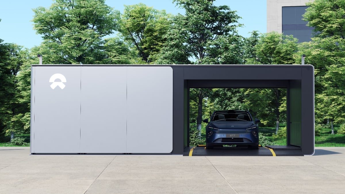 Rendering of a NIO ET7 sedan parked inside the open bay of a white NIO Power swap station among trees