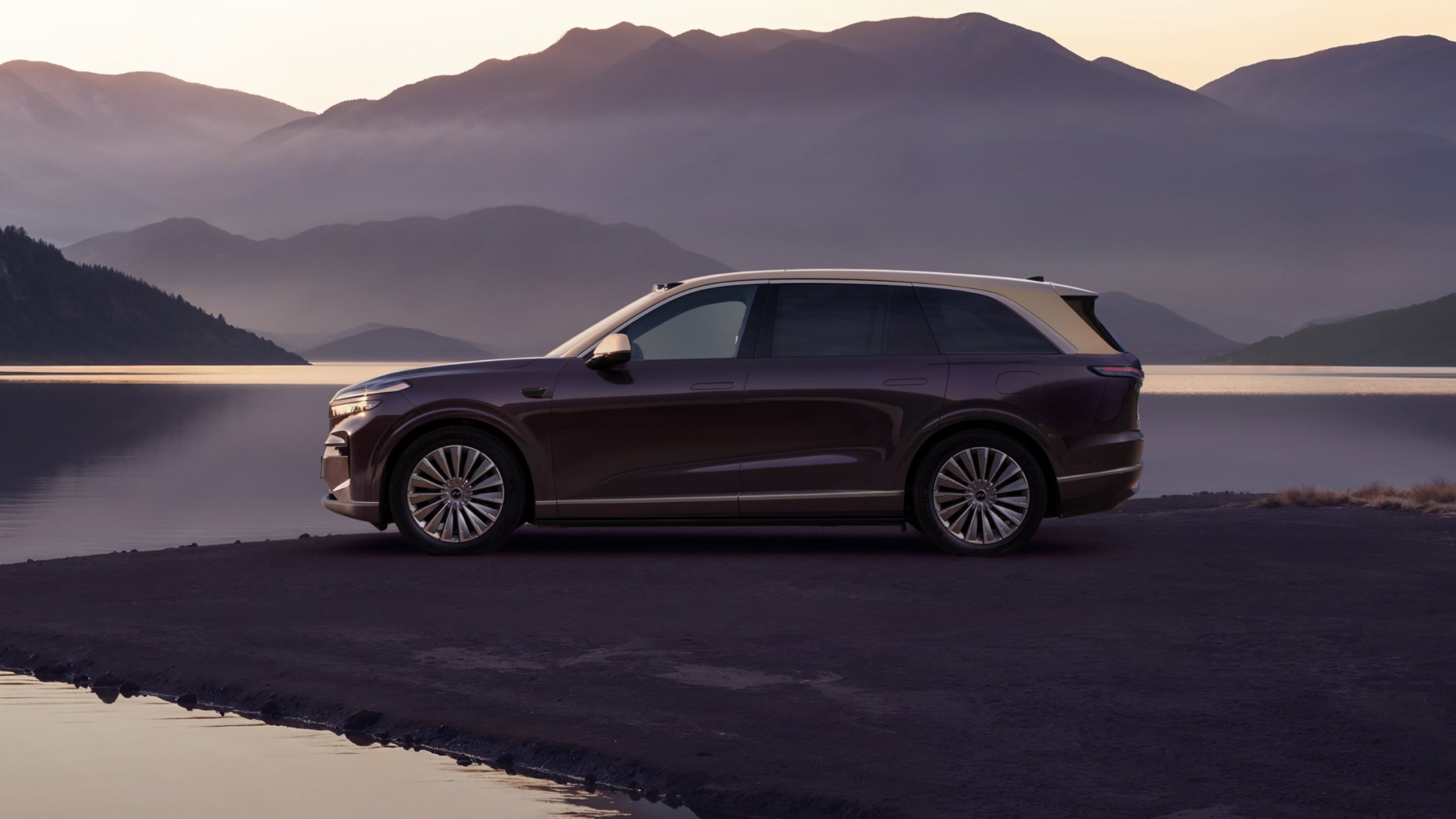Dark plum ONVO L90 large SUV in side profile beside a misty lake with mountains behind it at dusk