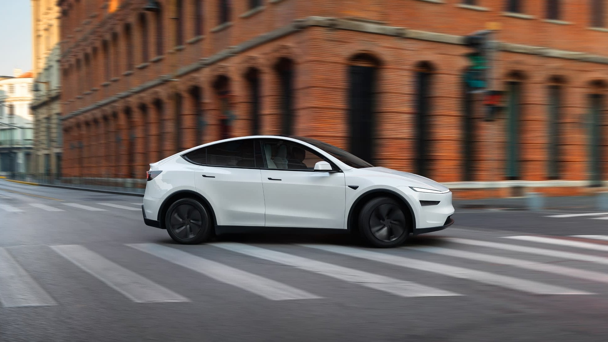 White Tesla Model Y in side profile crossing a city crosswalk past a red-brick building in China