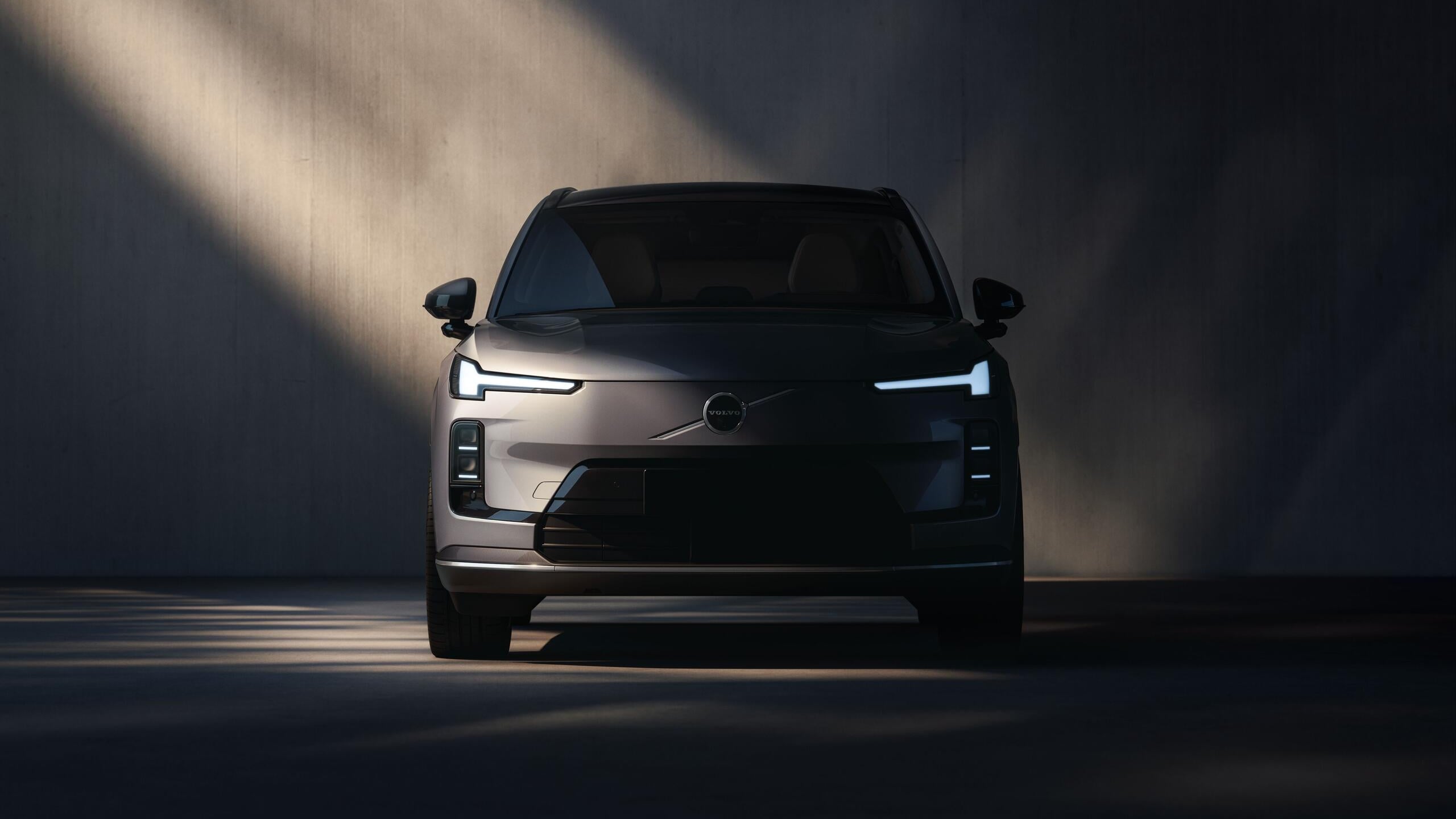 Volvo XC70 plug-in hybrid seen head-on in a dark studio, showing its closed shield grille and slim LED light bars