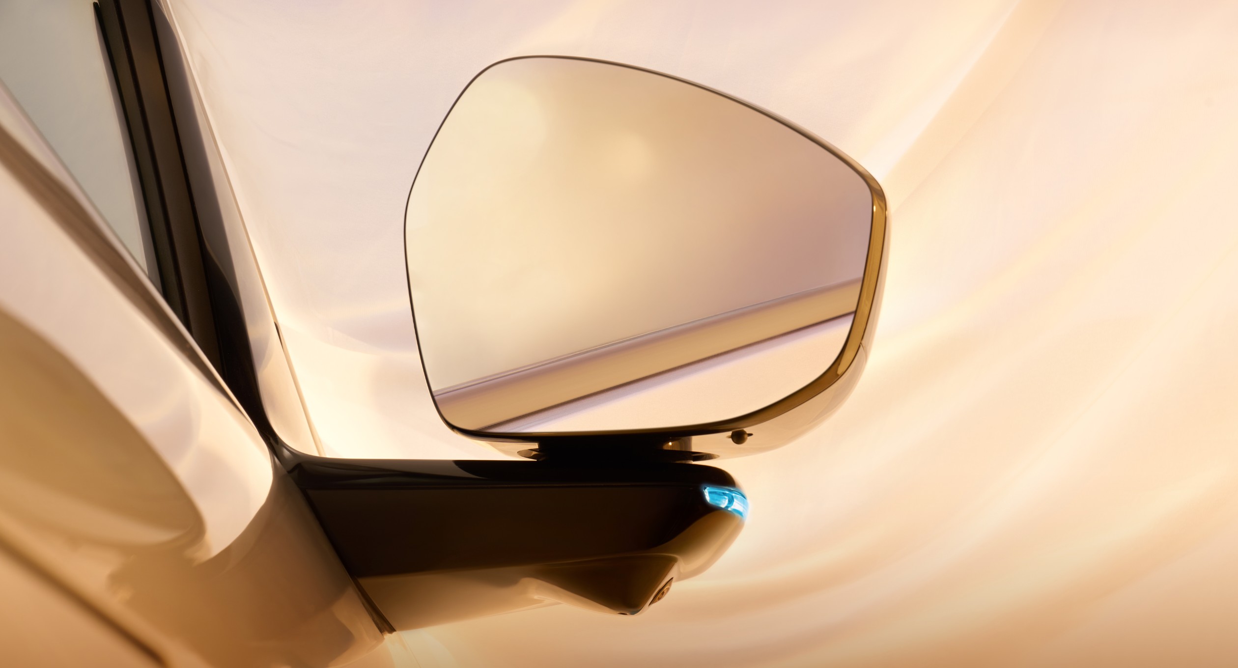 Close-up of an XPeng G7 door mirror with a small blue assisted-driving lamp lit on the underside of the mirror arm