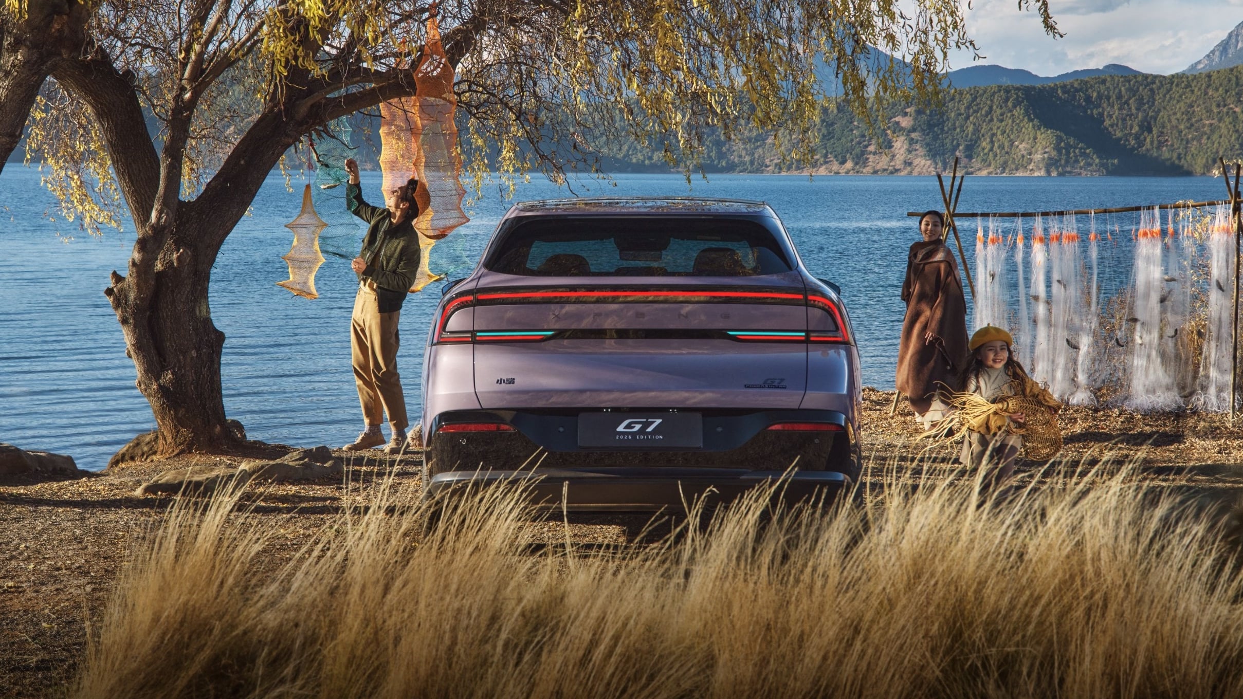 Rear view of a purple XPeng G7 parked by a lake, with teal assisted-driving indicator strips lit in its tail lamps