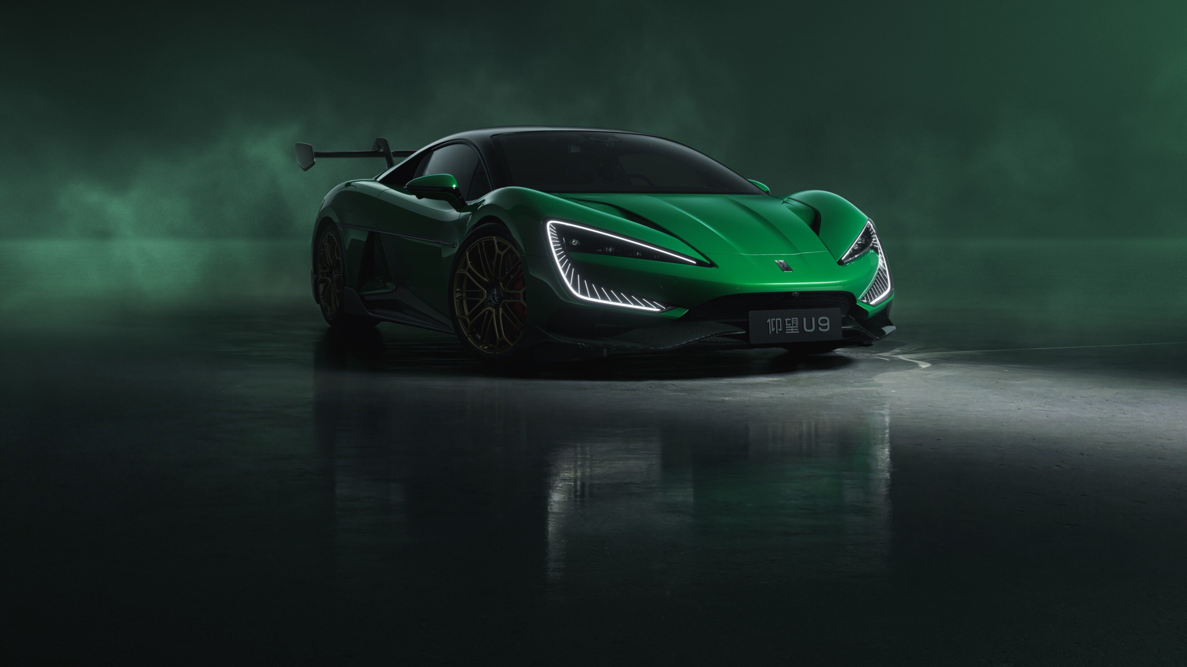 Green Yangwang U9 electric supercar front three-quarter view with rear wing in a dark, fog-filled studio