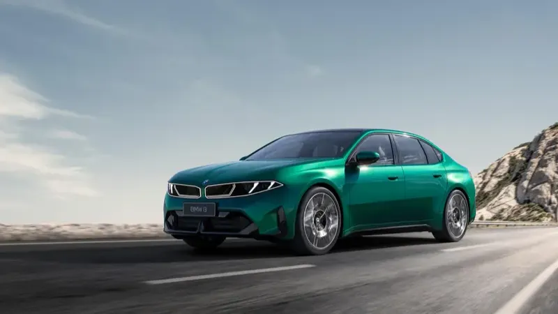 Green new-generation BMW i3 sedan in motion, showing its closed illuminated grille and sloped roofline